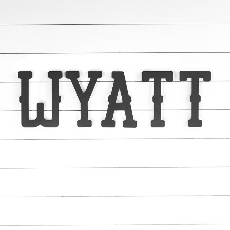 May include: Black wooden letters spelling out the name "WYATT" on a white wood background.