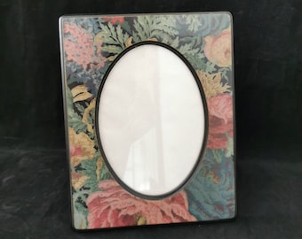 Peut inclure: Un cadre photo noir avec une ouverture ovale. Le cadre est décoré d'un motif floral dans des tons de rose, bleu, vert et jaune.