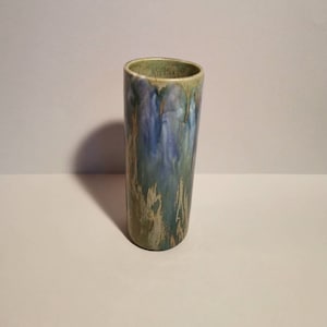 Op de afbeelding: Een hoge, cilindervormige keramische vaas met een glanzende afwerking. De vaas heeft een mix van blauwe, groene en gouden tinten, met een druipglazuureffect. De binnenrand is donkergroen. De vaas is ongeveer 20 cm hoog.