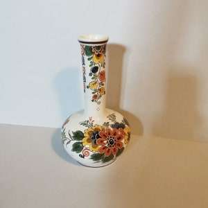 Könnte beinhalten: Eine weiße Keramikvase mit einem bauchigen Boden und einem langen, schlanken Hals. Die Vase ist mit einem bunten Blumenmuster in Orange-, Gelb-, Blau- und Grüntönen verziert.