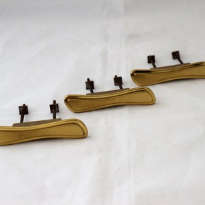 Könnte beinhalten: Drei goldfarbene Schranktürgriffe mit gebogenem Design und Schraubbefestigung.