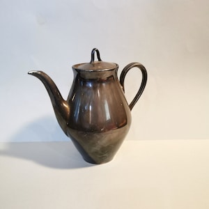 Op de afbeelding: Een zilverkleurige keramische theepot met een rond lichaam en een deksel. De theepot heeft een tuit en een handvat.