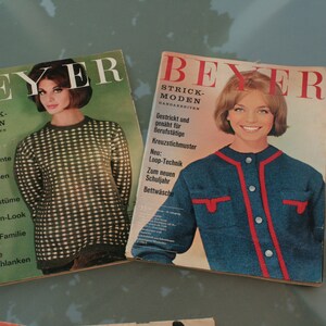May include: Two vintage knitting magazines with the title "BEYER STRICK-MODEN" on the cover. The magazines feature women wearing knitted sweaters and the text "Interessante neue Materialien, Kleider und Kostüme, Trachten-Look für die ganze Familie, Für die Vollschlanken, Gestrickt und gearbeitet für Berufstätige, Kreuzstichmuster, Neu: Loop-Technik, Zum neuen Schuljahr, Bettwäsche".
