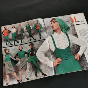 Könnte beinhalten: Eine Vintage-Modemagazin-Seite mit Damenbekleidung. Die Outfits umfassen grüne, orangefarbene und graue Ensembles. Ein Model trägt einen grünen Rock und eine Weste mit einer weißen Bluse und einem grünen Kopftuch. Der Text "DAS MODELL DES MONATS" ist sichtbar.