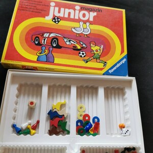 Puede incluir: Una caja de juego de mesa vintage "junior magazin" en rojo y amarillo. El arte de la caja presenta un coche de carreras, un jugador de fútbol y dados. Dentro, una bandeja blanca contiene varias piezas de juego de colores.