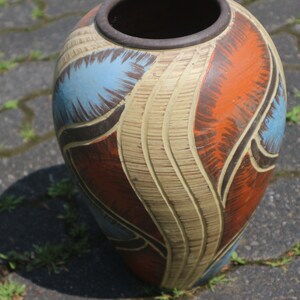 May include: A large, ceramic vase with a textured, cream-colored base and abstract designs in shades of blue, brown, and orange.