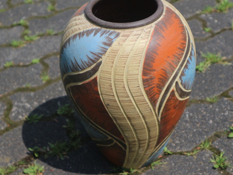 May include: A large, ceramic vase with a textured, cream-colored base and abstract designs in shades of blue, brown, and orange.