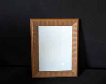 Peut inclure: Un cadre photo rectangulaire en bois avec une finition marron clair. Le cadre présente un motif texturé et strié sur les bords et un intérieur blanc. Le cadre est vide et posé sur une surface noire.