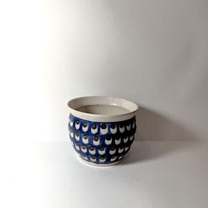 May include: A white ceramic planter with a blue and brown polka dot pattern. The planter is round and has a slightly flared rim.