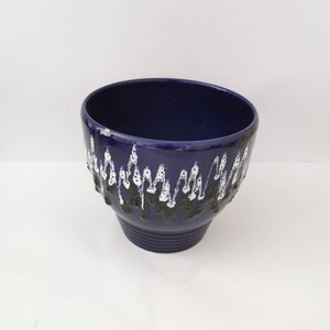 Puede incluir: Una maceta de cerámica azul oscuro con un diseño texturizado y ondulado en blanco y negro en el borde. La maceta tiene una forma ligeramente acampanada y una base acanalada, ideal para plantas de interior.