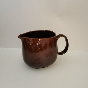 May include: A brown ceramic creamer pitcher with a rounded body and a handle. The pitcher is glazed with a glossy finish.