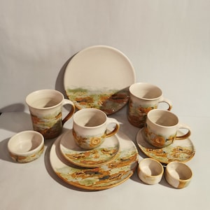Könnte beinhalten: Ein Set aus Keramikbechern und Untertassen mit weißem Hintergrund und braunen und grünen Mustern. Das Set enthält einen großen Teller mit einem ähnlichen Muster.