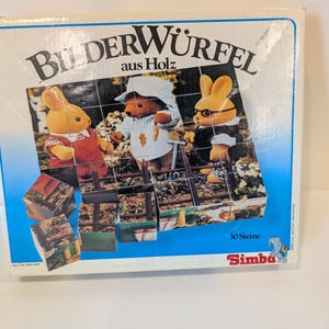May include: A vintage children's puzzle box with the title "Bilderwürfel aus Holz" and the Simba logo. The box features an image of three anthropomorphic animal characters, including two rabbits and a bear, and the puzzle pieces are visible.