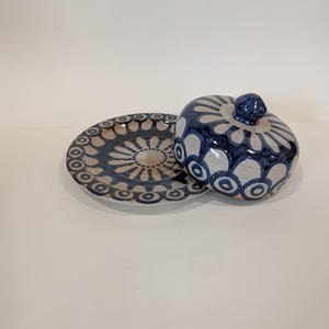 Peut inclure: Un beurrier en céramique blanche avec un motif floral bleu et blanc. Le beurrier a un couvercle et une assiette assortie.