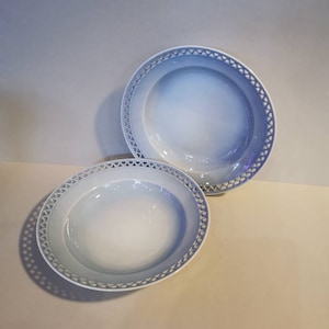 May include: Two white ceramic bowls with a blue lace trim. The bowls are empty and are sitting on a white surface.