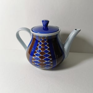 Puede incluir: Una tetera de cerámica azul y marrón con un patrón geométrico. La tetera tiene una tapa y un pico.