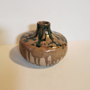 May include: A handmade ceramic vase with a rounded body and a narrow neck. The vase has a brown base with dark green and brown dripped glaze details. The interior of the neck is dark green.