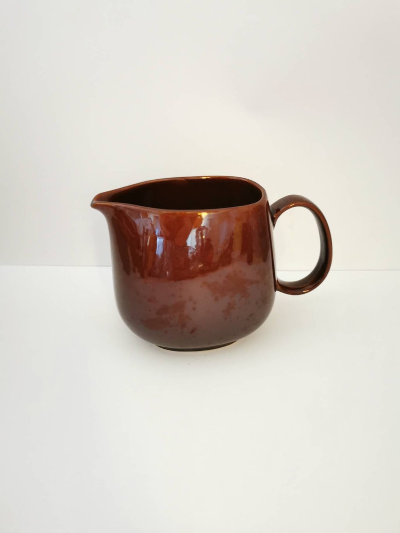 May include: A brown ceramic pitcher with a rounded body and a handle. The pitcher is glazed and has a smooth finish.