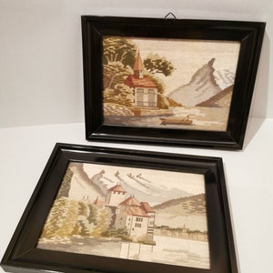 Könnte beinhalten: Zwei gerahmte Nadelbilder mit schwarzen Rahmen. Das obere Bild zeigt ein kleines Haus an einem See mit Bergen im Hintergrund. Das untere Bild zeigt ein Schloss an einem See mit Bergen im Hintergrund.