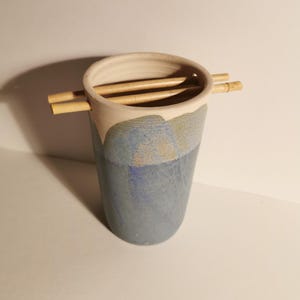 Könnte beinhalten: Ein blauer und weißer Keramik-Stäbchenhalter mit zwei Holzstäbchen, die obenauf liegen.