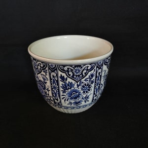 Könnte beinhalten: Ein weißer Keramiktopf mit einem blauen und weißen Blumenmuster. Der Topf hat einen abgerundeten Boden und eine breite Öffnung.
