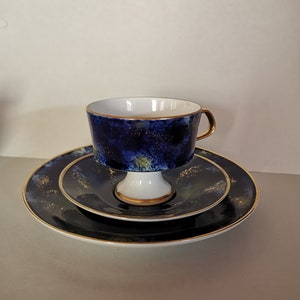 Puede incluir: Un juego de taza y platillo de té azul y dorado con un diseño de noche estrellada. La taza tiene una base de pedestal y un borde dorado.