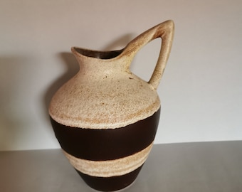 Może przedstawiać: Biały ceramiczny wazon w brązowe pasy. Wazon ma fakturowaną powierzchnię i unikalny uchwyt.