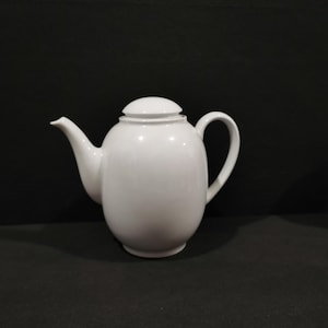 May include: A white ceramic teapot with a rounded body and a lid. The teapot has a spout and a handle.