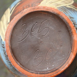 May include: The bottom of a brown ceramic vase with a blue and yellow design. The vase is marked with the text "325" and "Handarbeit".