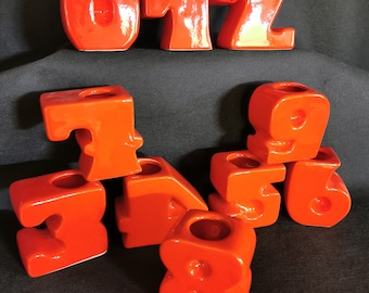 May include: A set of orange ceramic candle holders shaped like the numbers 0, 1, 2, 3, 4, 5, 6, 7, 8, and 9.
