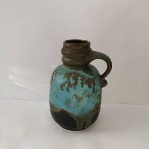 Puede incluir: Un jarrón de cerámica azul y marrón con asa. El jarrón tiene un esmalte texturizado y un efecto de goteo.