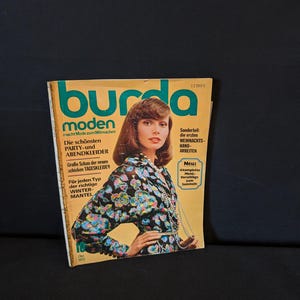 Peut inclure: Un magazine Burda Moden vintage d'octobre 1972, avec une femme en couverture. Le magazine a une couverture jaune et verte avec du texte allemand et des images de modèles de mode. La mannequin de couverture porte un haut à imprimé floral.