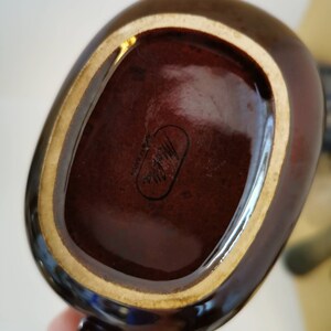 May include: A brown ceramic mug with a gold rim and a black handle. The bottom of the mug has a black oval sticker with the text "Made in Japan" inside.