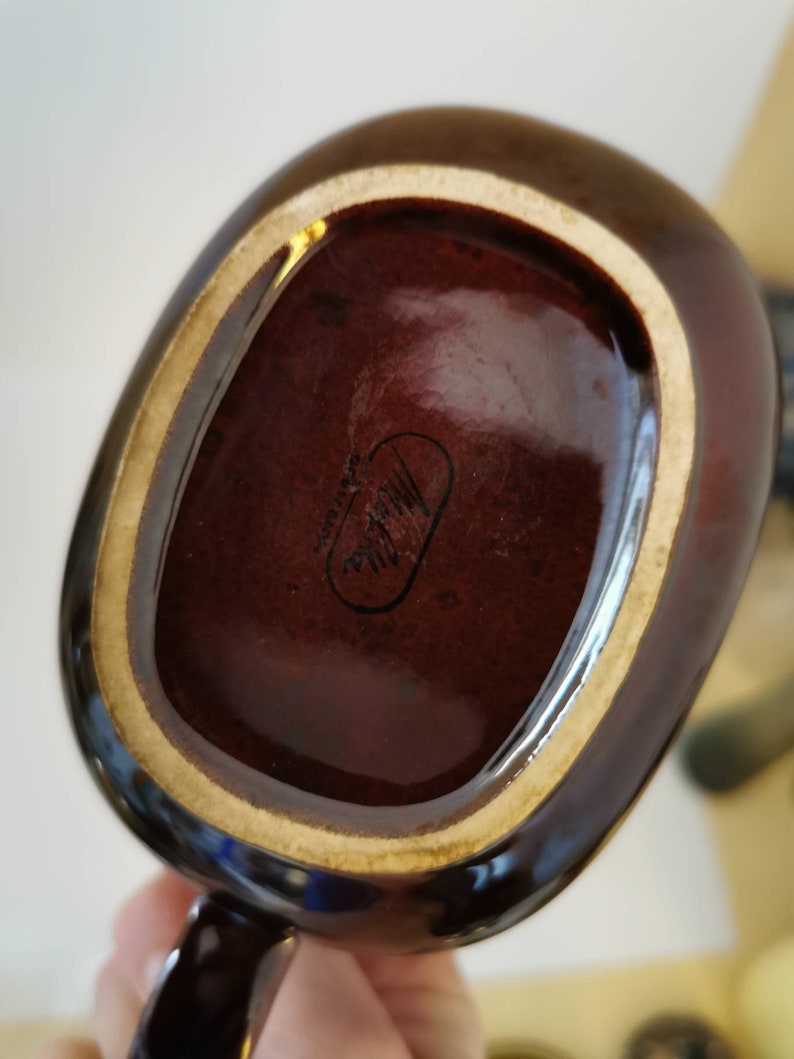 May include: A brown ceramic mug with a gold rim and a black handle. The bottom of the mug has a black oval sticker with the text "Made in Japan" inside.