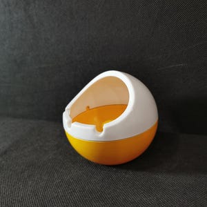 Könnte beinhalten: Ein gelber und weißer Aschenbecher aus Keramik in Form einer Halbkugel. Der Aschenbecher hat einen weißen Rand und ein gelbes Innere.