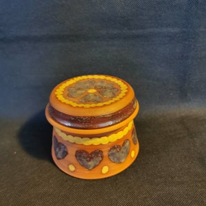 Peut inclure: Un petit pot rond en céramique avec un couvercle. Le pot est décoré d'un motif floral brun et jaune et d'un motif de cœur brun et jaune. Le pot est de couleur brun clair.
