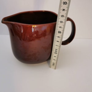 May include: A brown ceramic pitcher with a rounded body and a handle. The pitcher is about 17 cm tall.