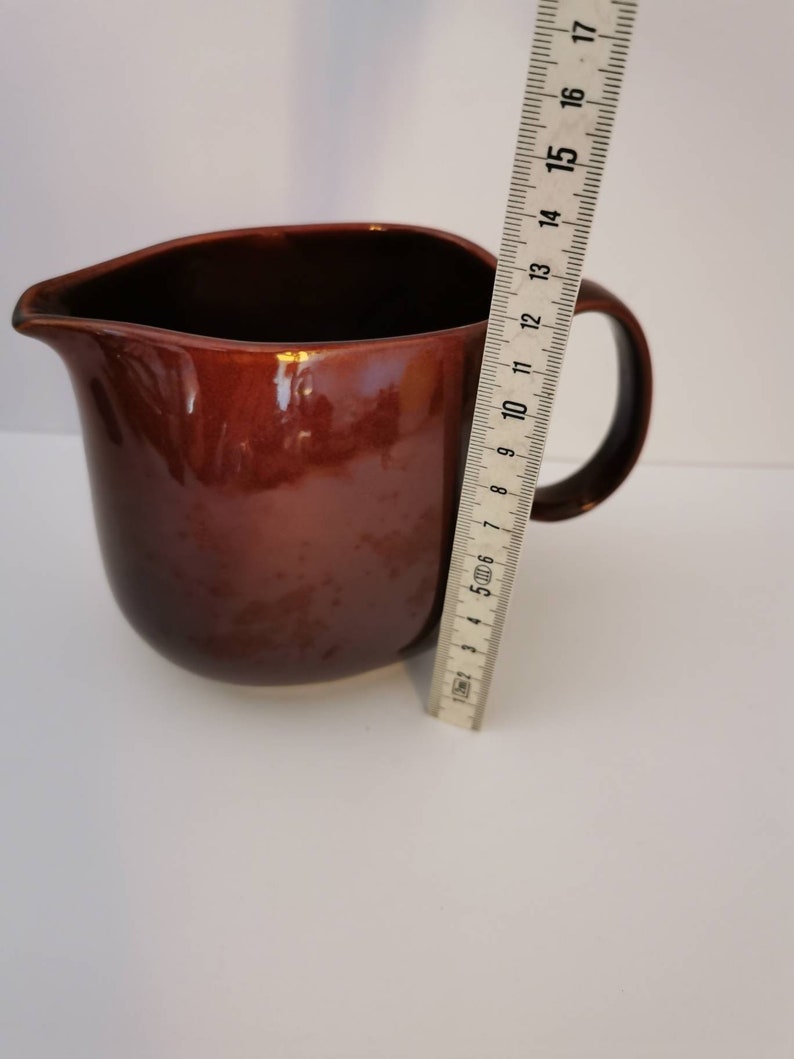 May include: A brown ceramic pitcher with a rounded body and a handle. The pitcher is about 17 cm tall.