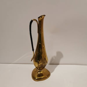 Può includere: Un vaso vintage in ottone con un corpo sottile e allungato e un manico curvo con un cordoncino nero. Il vaso ha una base svasata e un'apertura stretta. L'ottone ha una calda tonalità dorata.