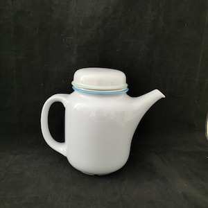 Puede incluir: Tetera de cerámica blanca con un borde azul y verde alrededor de la tapa. La tetera tiene un cuerpo redondeado y un pico en el lado derecho.