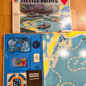 Puede incluir: Un juego de mesa vintage llamado "TEUFELS-DREIECK" con temática náutica. La caja muestra barcos en un mar tormentoso. En el interior, hay un tablero de juego, piezas y instrucciones. El juego está diseñado para jugadores de 8 a 80 años.