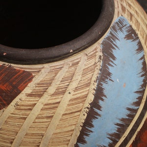 May include: A large, round, ceramic pot with a brown rim and a decorative design. The design features brown, white, and blue brushstrokes.