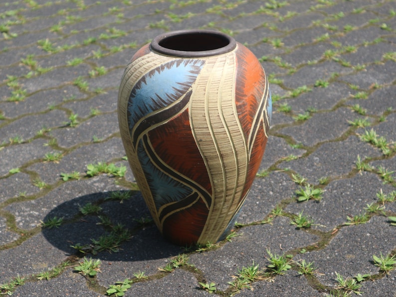 May include: A ceramic vase with a geometric design in shades of blue, brown, orange, and white. The vase has a rounded shape and a wide opening.