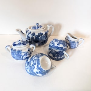 Può includere: Un servizio da tè in miniatura in porcellana blu e bianca. Il set comprende una teiera con coperchio, due zuccheriere coperte, due tazze da tè e una lattiera. Il servizio da tè presenta un classico motivo blu salice.