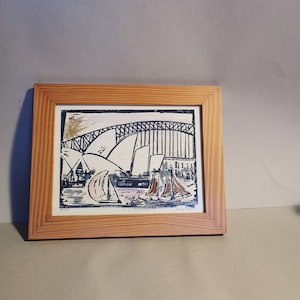 Könnte beinhalten: Ein gerahmter Druck einer farbenfrohen Illustration des Opernhauses von Sydney und der Harbour Bridge von Sydney mit Segelbooten im Vordergrund. Der Druck ist mit "To the Lovers of Sydney" betitelt und von "David Roberts" signiert.