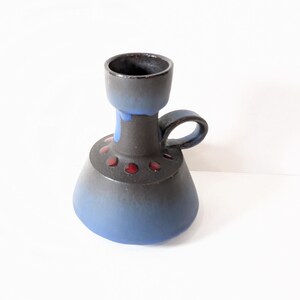 Könnte beinhalten: Ein blauer und schwarzer Kerzenhalter aus Keramik mit einem roten und schwarzen Design. Der Halter hat einen Griff und eine breite Basis.