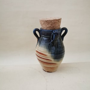 Può includere: Un piccolo vaso in ceramica dipinto a mano con un tappo di sughero. Il vaso ha una smaltatura blu, bianca e marrone con un motivo a spirale.
