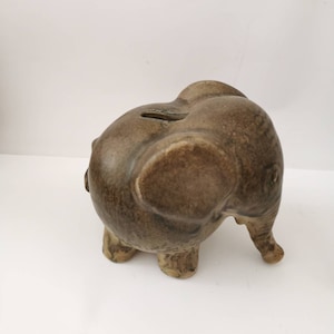 Könnte beinhalten: Eine braune Keramik-Sparbüchse in Form eines Elefanten mit einer strukturierten Oberfläche. Der Elefant steht auf allen vieren und hat seinen Rüssel erhoben.