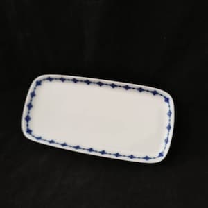 Può includere: Un piatto da portata rettangolare bianco con un bordo a forma di diamante blu.