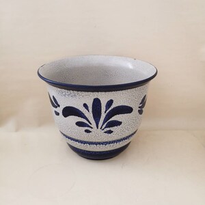 Può includere: Un vaso di ceramica bianca con un motivo floreale blu. Il vaso ha una superficie testurizzata e un bordo largo.